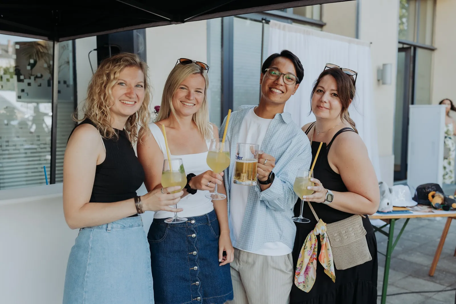 Vier Kolleg:innen stoßen beim Sommerfest mit Getränken an